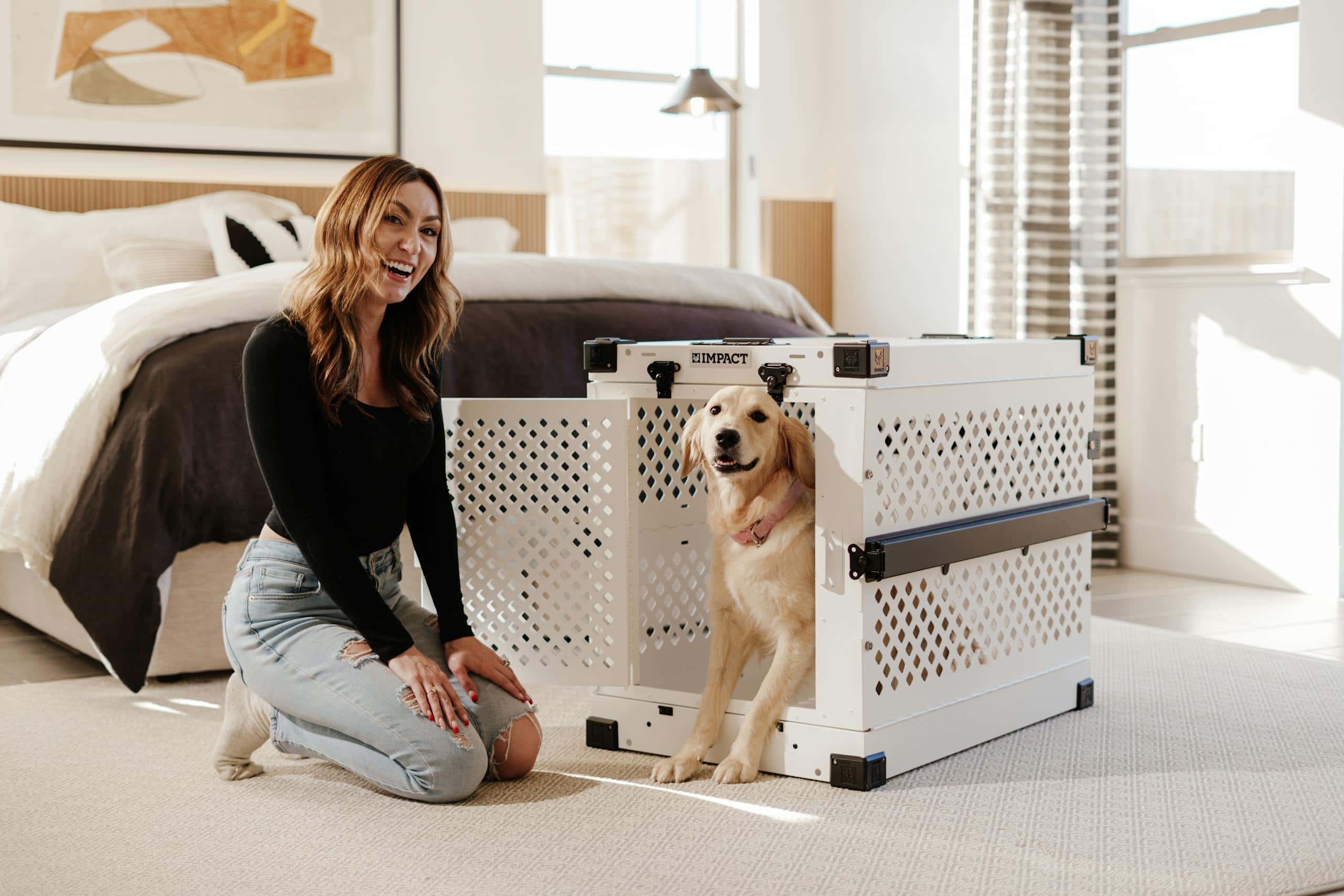 A cheerful woman poses with a golden retriever next to a premium dog crate in a stylish bedroom.